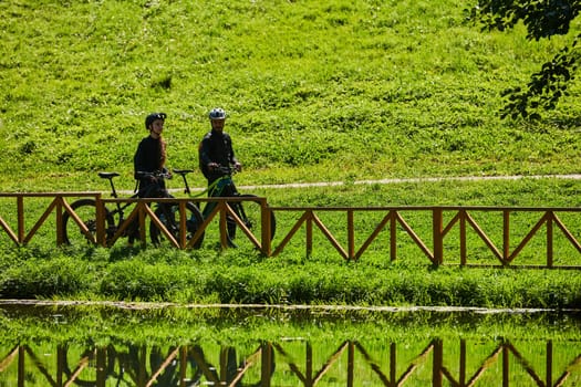 A blissful couple, adorned in professional cycling gear, enjoys a romantic bicycle ride through a park, surrounded by modern natural attractions, radiating love and happiness.