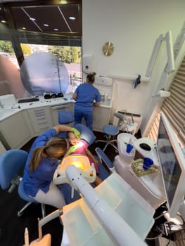 Dentist examines with a mirror under the lamp a little girl sitting with her mouth open. High quality photo