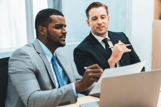 African male leader explain strategy while show solution to professional project manager by pointing at document, using laptop. Skilled business team brainstorming idea. Business meeting. Ornamented.