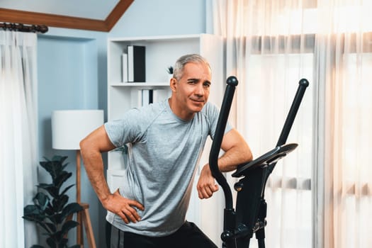 Active senior man running on elliptical running machine at home portrait as fitness healthy lifestyle and body care after retirement for pensioner. Clout