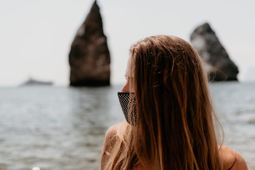 Woman travel sea. Young Happy woman in a long red dress posing on a beach near the sea on background of volcanic rocks, like in Iceland, sharing travel adventure journey