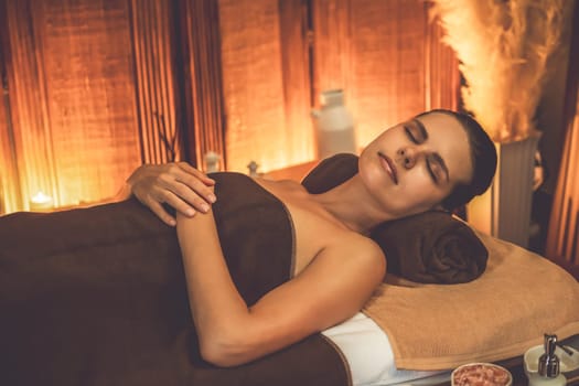 Caucasian woman customer enjoying relaxing anti-stress spa massage and pampering with beauty skin recreation leisure in warm candle lighting ambient salon spa at luxury resort or hotel. Quiescent