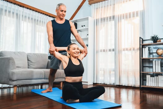 Happy active senior couple in sportswear being supportive and assist on yoga posture together at home. Healthy senior man and woman lifestyle with yoga exercise. Clout