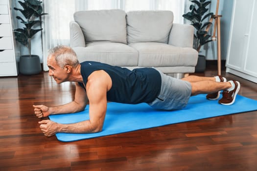 Athletic and sporty senior man planking on fitness exercising mat at home exercise as concept of healthy fit body lifestyle after retirement. Clout
