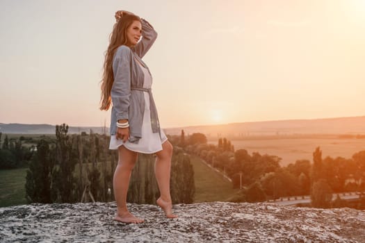 Romantic beautiful bride in white dress posing with sea and mountains in background. Stylish bride standing back on beautiful landscape of sea and mountains on sunset