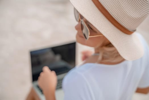 Freelance women sea working on the computer. Good looking middle aged woman typing on a laptop keyboard outdoors with a beautiful sea view. The concept of remote work