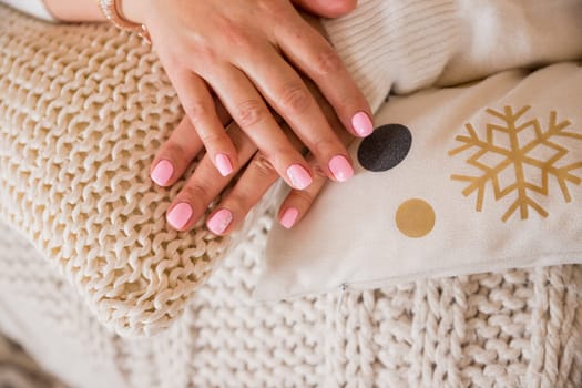 Female hand with beautiful natural manicure - pink nude nails on pale pink fluffy fabric, textile background