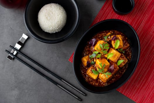 Mapo Tofu bowl with side sauces on black stone table