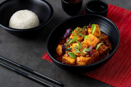 Mapo Tofu bowl with side sauces on black stone table