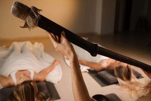 girls, lying on the floor, relax under the sound instrument of the rain staff in the fitness room.