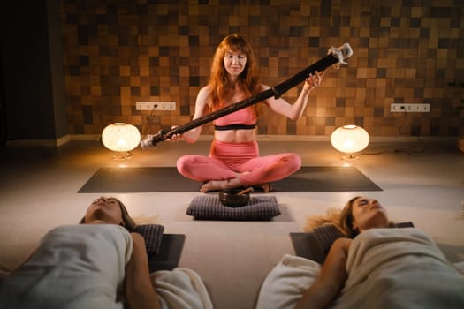 girls, lying on the floor, relax under the sound instrument of the rain staff in the fitness room.