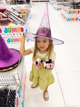 Little girl trying on pointy purple witch hat in shop. High quality photo
