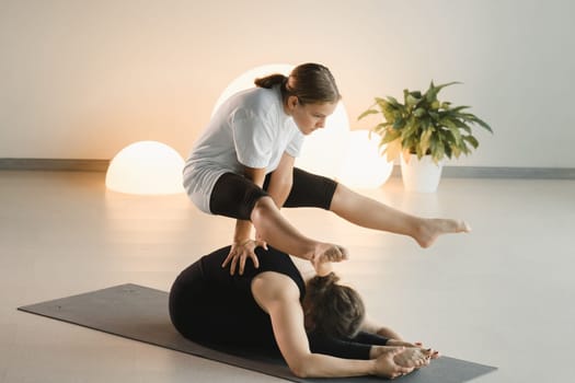 Mom and teenage daughter do gymnastics together in the fitness room. A woman and a girl train in the gym.