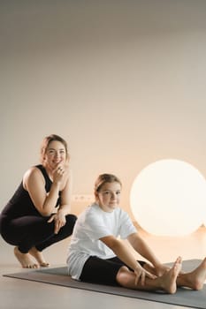 Mom and teenage daughter do gymnastics together in the fitness room. A woman and a girl train in the gym.