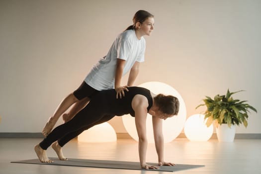 Mom and teenage daughter do gymnastics together in the fitness room. A woman and a girl train in the gym.