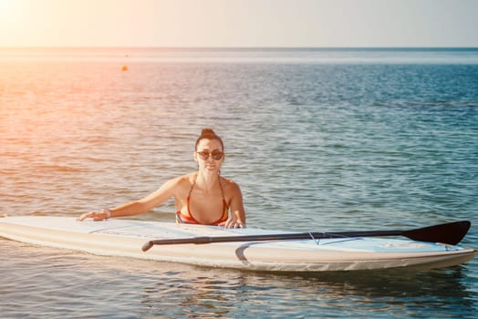 Sea woman sup. Silhouette of happy middle aged woman in rainbow bikini, surfing on SUP board, confident paddling through water surface. Idyllic sunset. Active lifestyle at sea or river