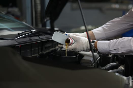 Auto mechanic pours oil into car engine from cans of oil. Oil change in car concept