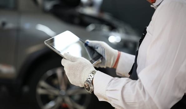 Male master locksmith holds tablet and performs car diagnostics. Apps for car repair concept