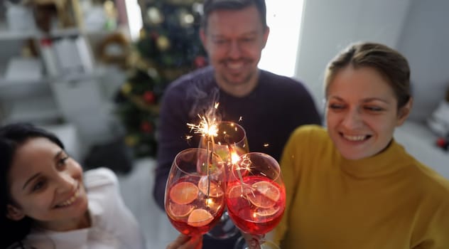 Cheerful happy people hold alcoholic cocktails with sparklers closeup. Holiday New Year party or birthday