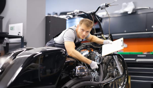 Male mechanic diagnoses modern motorcycle in service center. Concept of vehicle maintenance and transport insurance