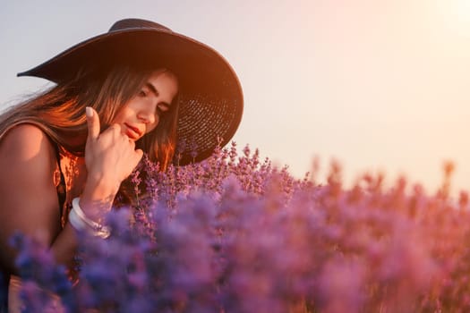 Close up portrait of young beautiful woman in a white dress and a hat is walking in the lavender field and smelling lavender bouquet.