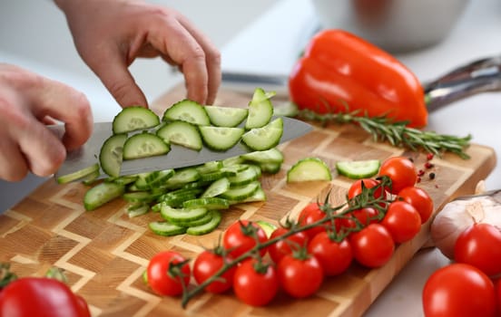 Cutting vegetables with knife for cooking on board. Cucumber tomatoes cooking salad