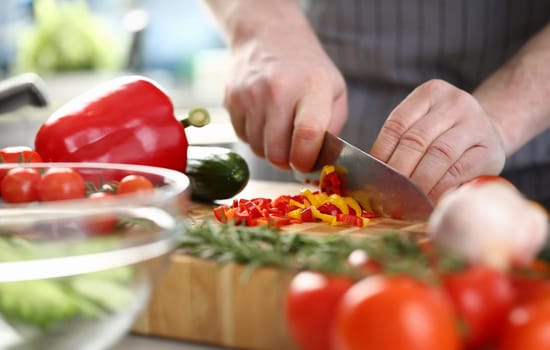 Hands of cook cut yellow and red peppers on cutting board with other vegetables on table in kitchen. Cooking fresh vitamin tasty salad concept