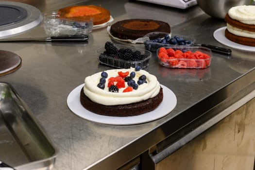 pastry chef artisan making strawberry and blueberry drip frosted cake for a birthday in professional kitchen