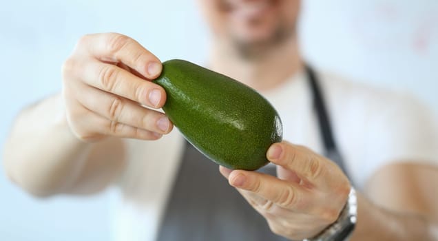 Male cook holds green fresh tasty avocado in hands. Natural fresh organic exotic fruits and healthy food concept