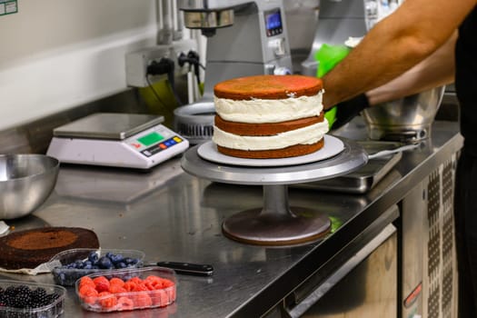 pastry chef artisan making strawberry and blueberry drip frosted cake for a birthday in professional kitchen
