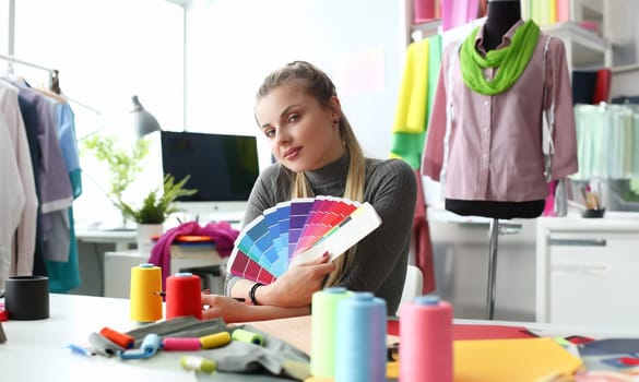 Female fashion designer seamstress working in studio holding color palette. Selection and choice of color solution in concept clothing collection