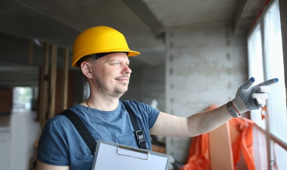 Male builder in helmet looks out window at construction site. Foreman foreman and foreman of construction projects concept