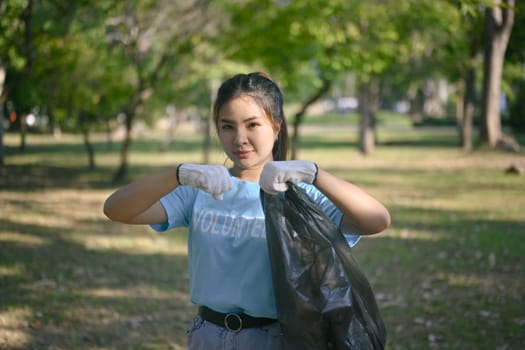 Pretty female volunteer collecting forest garbage and looking at camera. World Environment day concept.