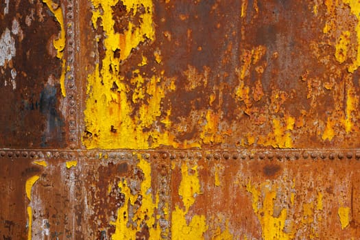 beautifully rusted rivetted sheet metal with leftovers of yellow paint texture and full-frame flat background.