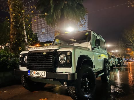White SUV stands in the parking lot under a street lamp. Logo: Land Rover. High quality photo