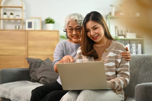 Happy mature mother and adult daughter using laptop surfing internet or shopping via internet at home.