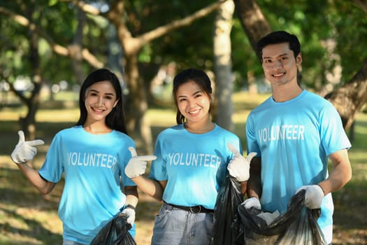 Group of happy volunteers with garbage bags cleaning area in park. Collaboration, charity and recycling concept.
