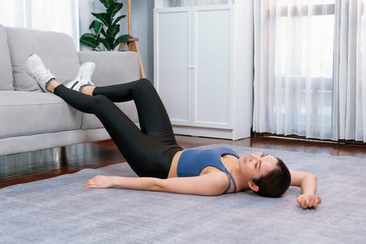 Young attractive asian woman in sportswear lies on the floor and doing sit-ups on the crouch, aiding targeting on abs muscle for effective home exercise routine. Vigorous