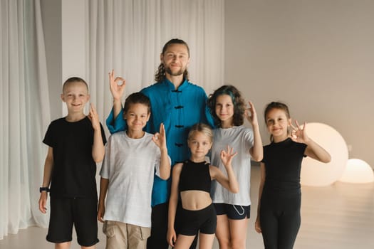 A joint portrait of a yoga coach and children standing in a fitness room.