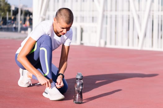 young sporty woman tying her running shoes before her workout, concept of healthy and active lifestyle, copy space for text