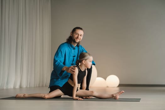 A yoga instructor in training helps a child to do exercises in the gym.