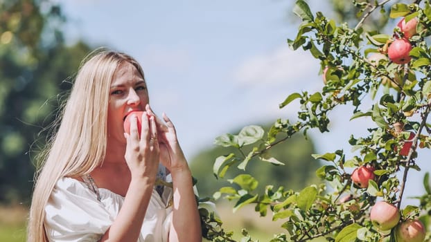A young woman plucks an apple from a tree and eats it