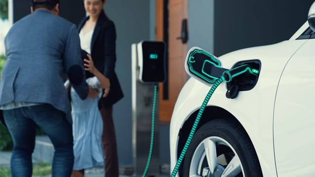 Modern family with young girl recharge electric car, EV charger from home charging station plugged in EV car in house garage. Smart and futuristic home energy infrastructure. Peruse