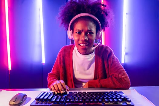 Gaming streamer, African girl playing online fighting with Esport skilled team wearing headphones in neon color lighting room. Talking other players planing strategies to win competitors. Tastemaker.