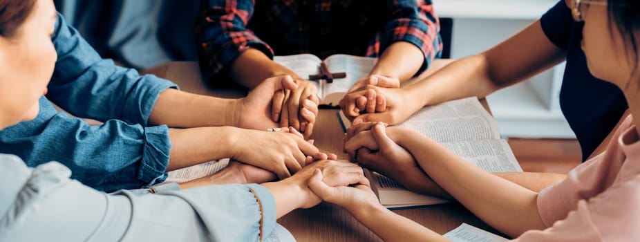 Cropped image of diversity people hand praying together at wooden church on bible book while hold hand together with believe. Concept of hope, religion, faith, god blessing concept. Burgeoning.