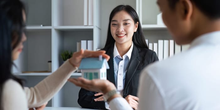 Young Asian couple making contract with house sale agency. man and his wife sitting signing the contract next to him looking the contract document with smile. real estate agreement successful concept.