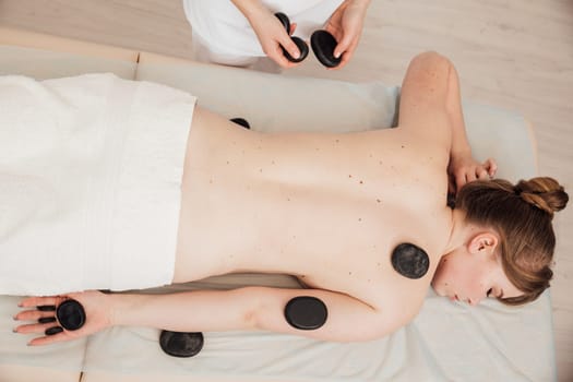 The masseur gives a back massage with stones to the client in the Health room