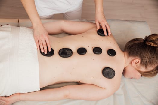 The masseur gives a back massage with stones to the client in the Health room