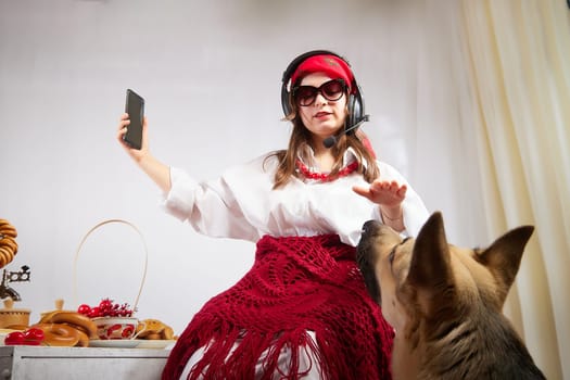 Young girl in red scarf, large headphones with microphone and black glasses and big shepherd dog. Woman who is radio or television presenter, female telecom operator, blogger or Freelancer and animal