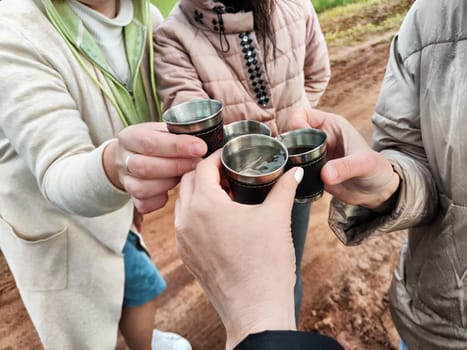 Women's hands with small cups, glasses or glasses are pushed together. Celebrating something outdoors at a campsite. Alcohol and vodka on holiday